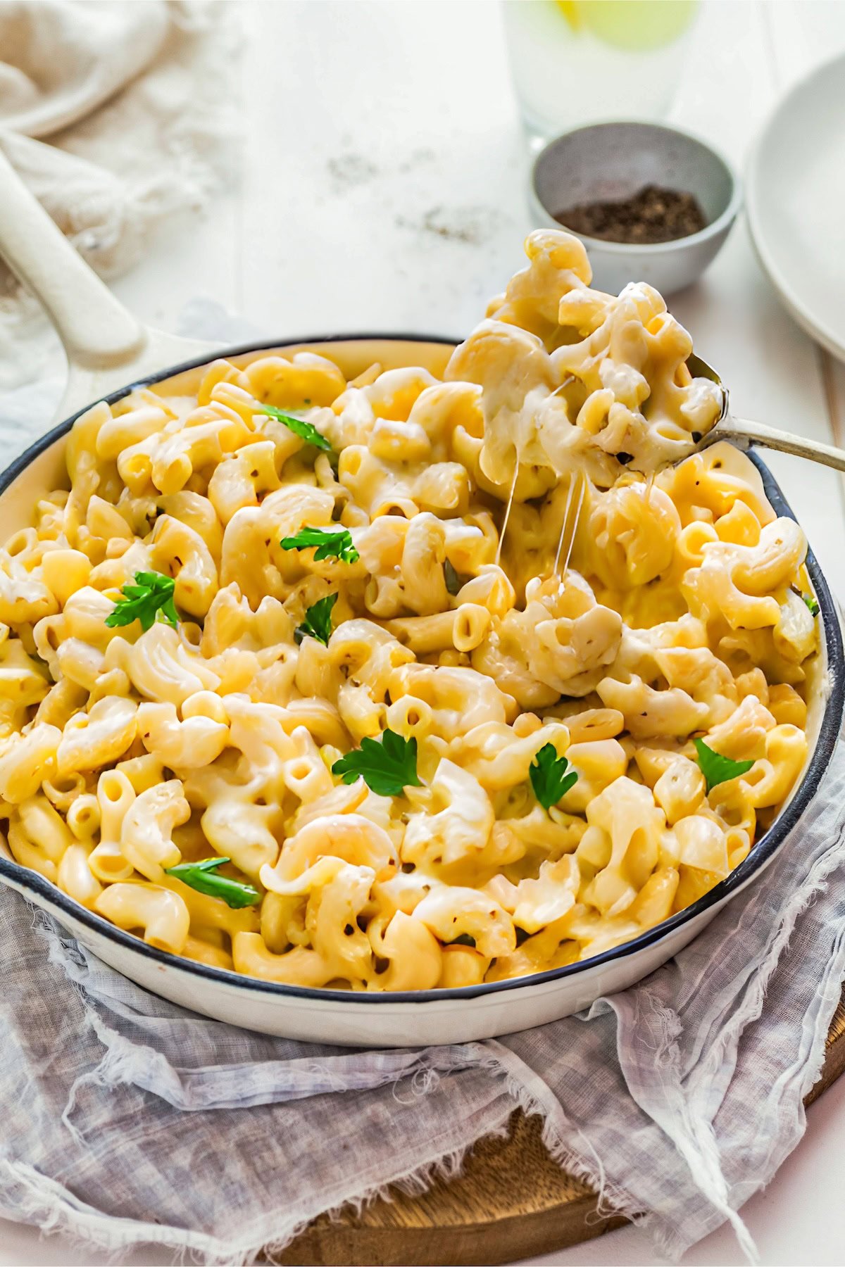 A spoon is lifting a cheesy bite of macaroni from a full skillet. 