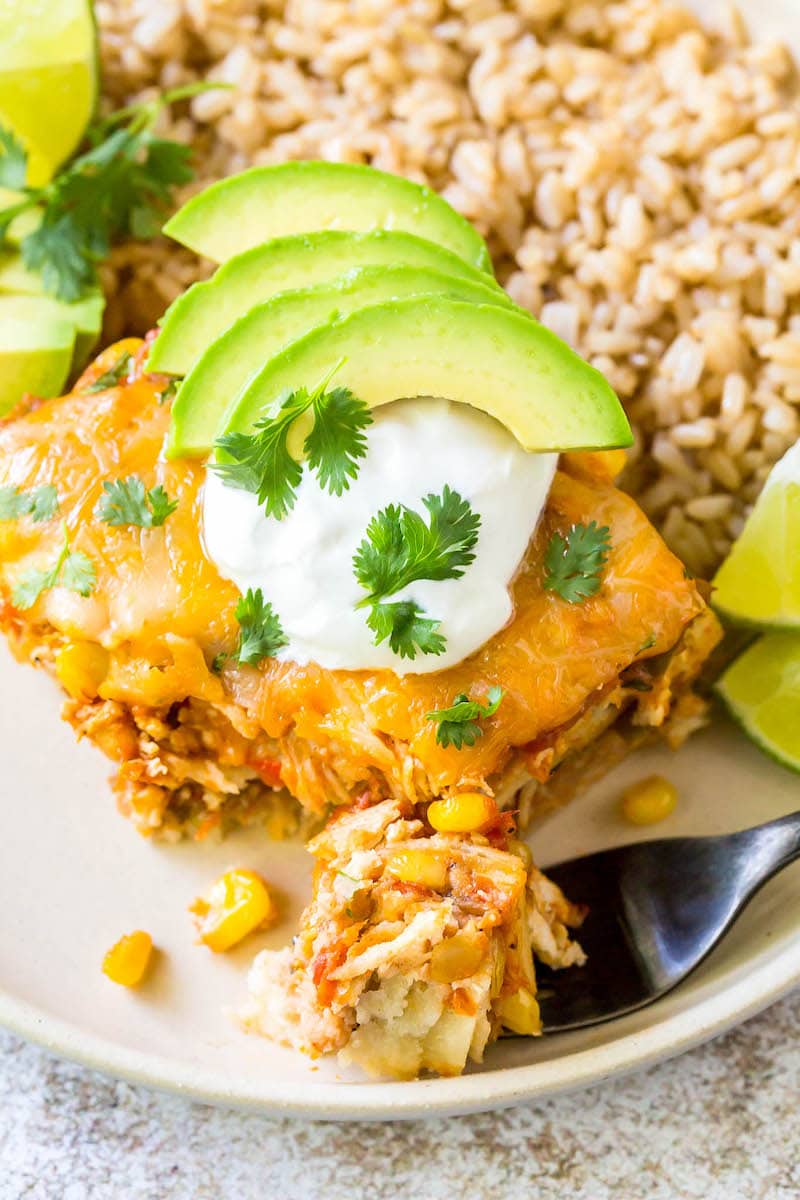 Mexican casserole topped with avocado sour cream and cilantro and served on a plate.