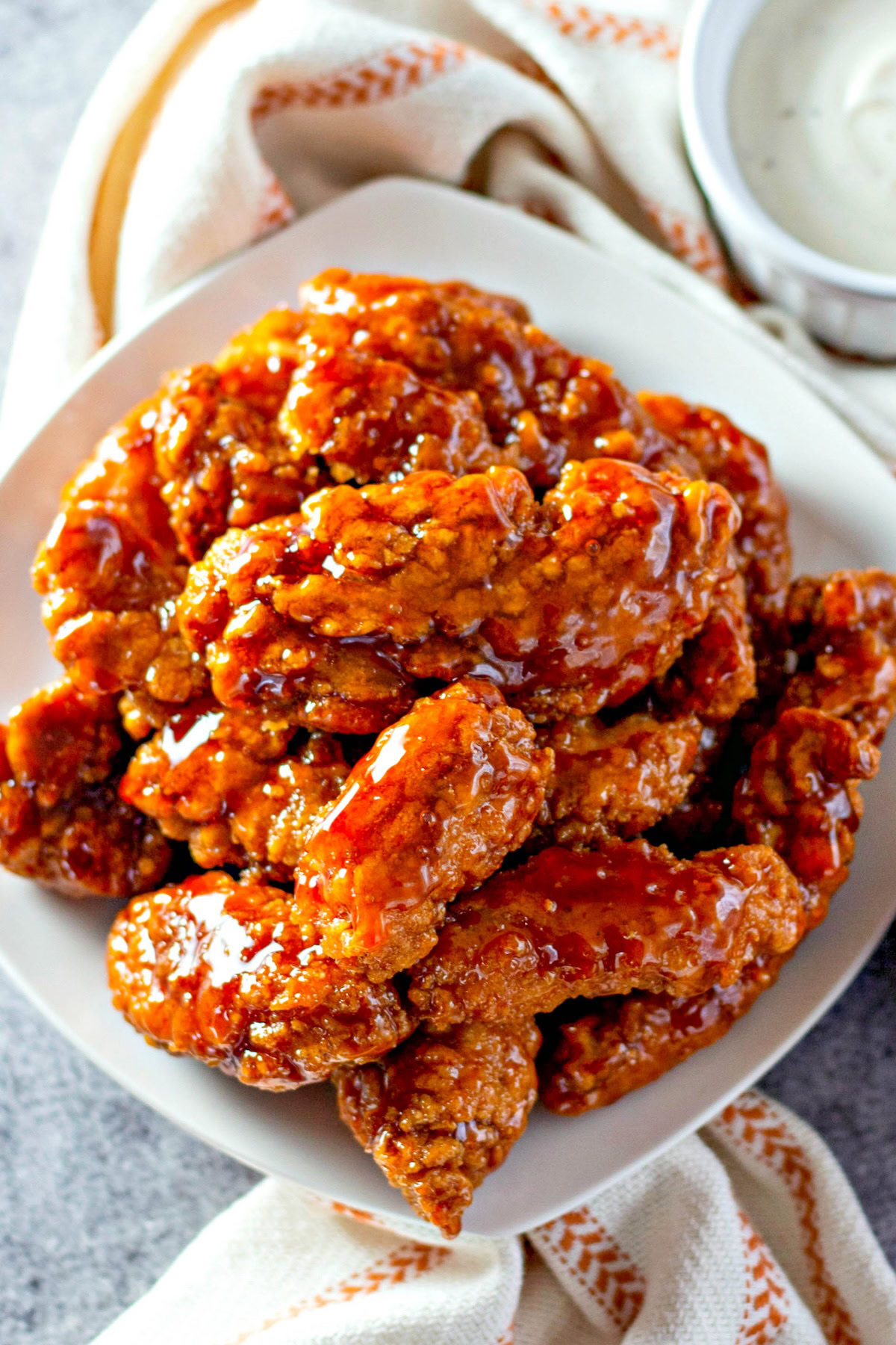 A white plate is piled high with saucy chicken tenders. 