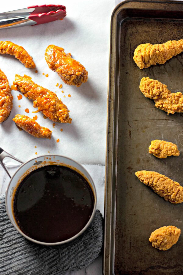 Crispy, golden chicken tenders are being coated in spicy sweet sauce. 