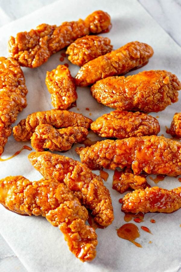 Sticky chicken tenders tossed in sauce on parchment paper.