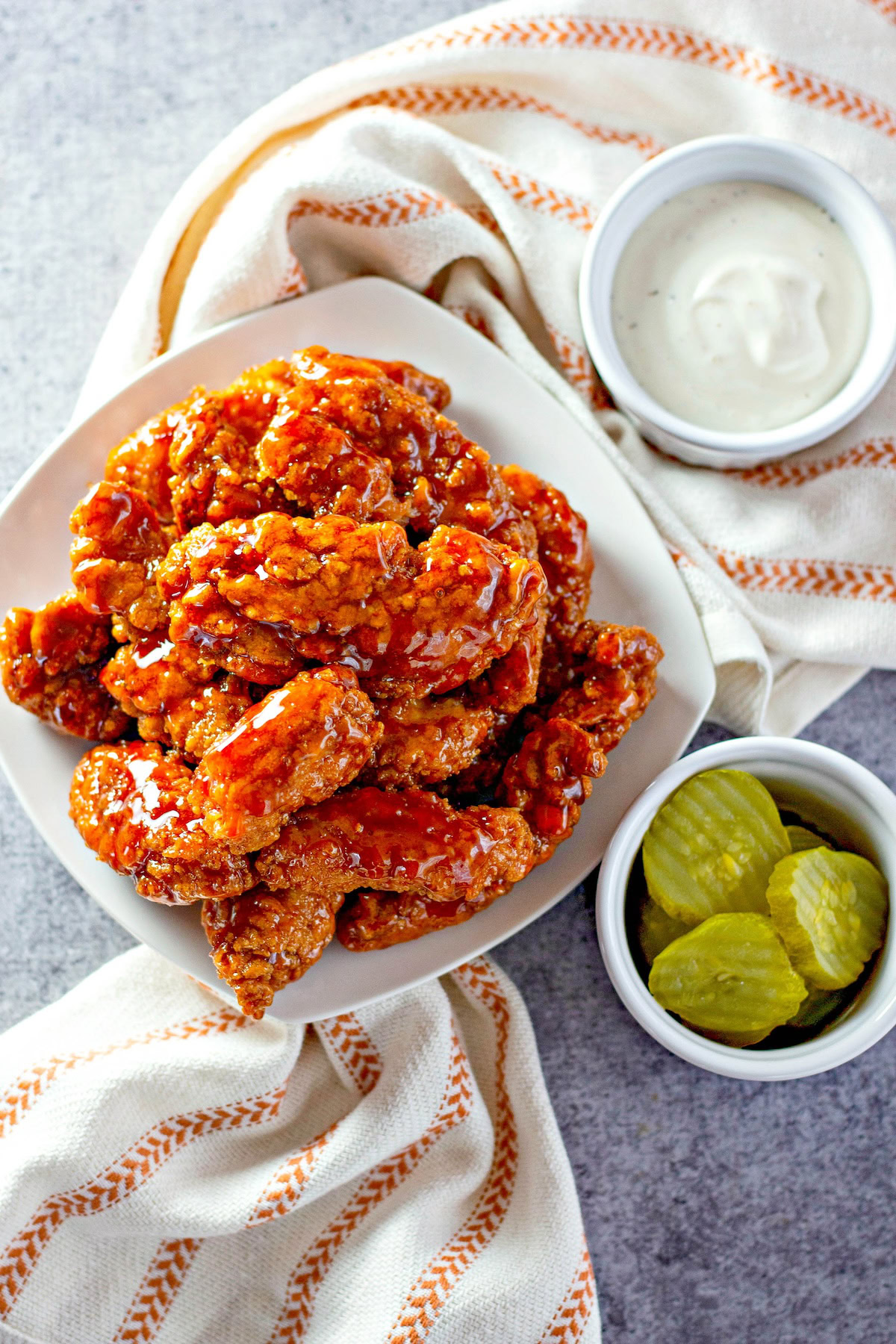 Sticky chicken strips are placed next to sliced pickles and ranch dressing. 