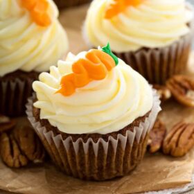 Three carrot cake cupcakes with a carrot on top.