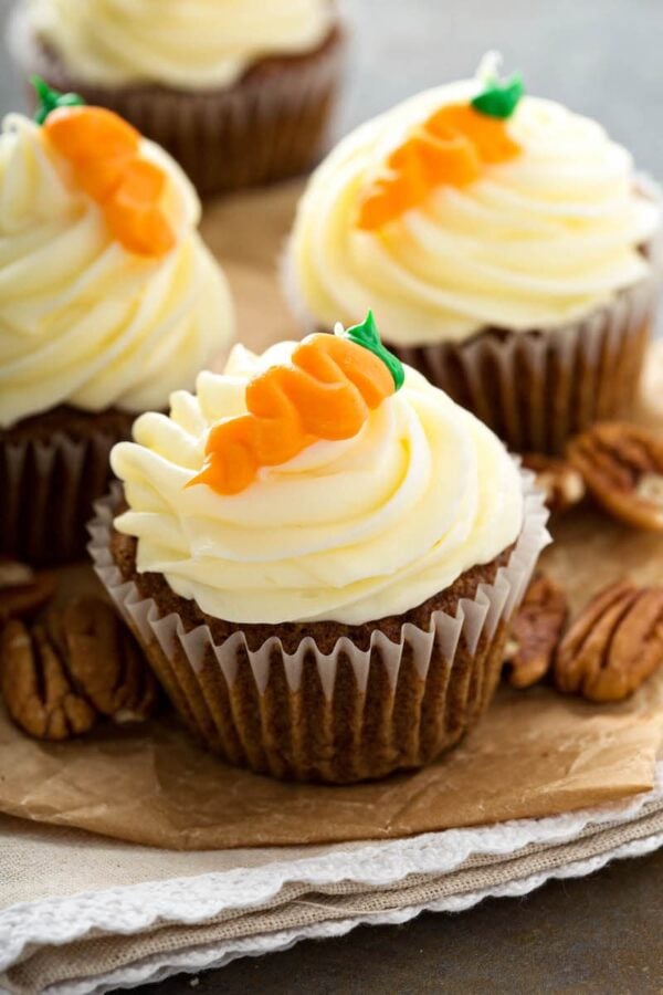 Three carrot cake cupcakes with a carrot on top.