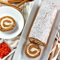 A sliced carrot cake roll with one slice on a plate.