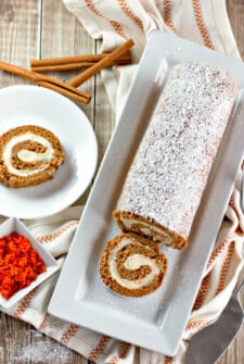 A sliced carrot cake roll with one slice on a plate.