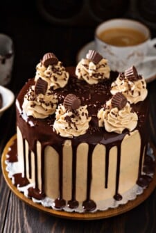 A frosted peanut butter chocolate cake is topped with sprinkles, candy and chocolate sauce.