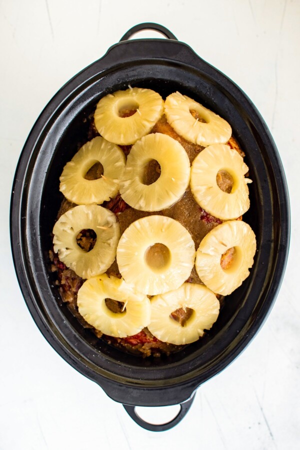 Ham in a crockpot covered in pineapple slices.