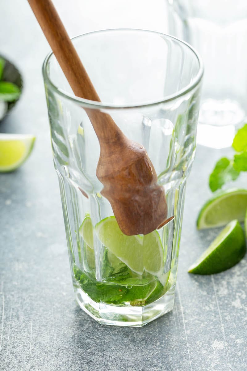 Clear glass with mint and lime in preparation to be muddled