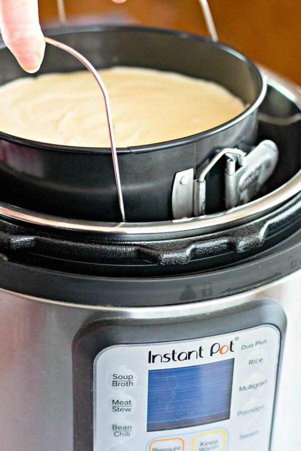 The cheesecake being lowered into the Instant Pot. 