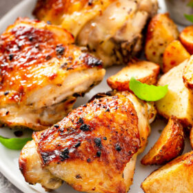 Perfectly baked chicken on a white plate with roasted potatoes.