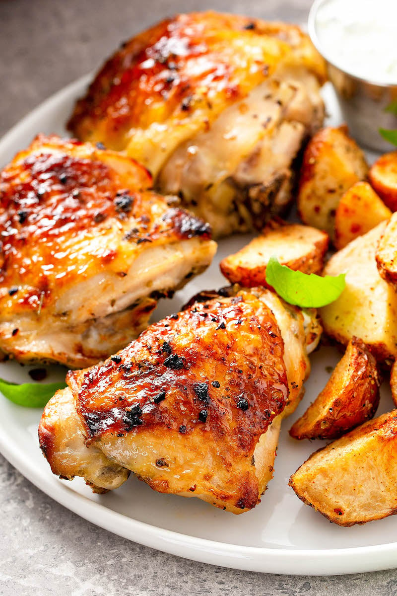 Baked chicken on a white plate with roasted potatoes.