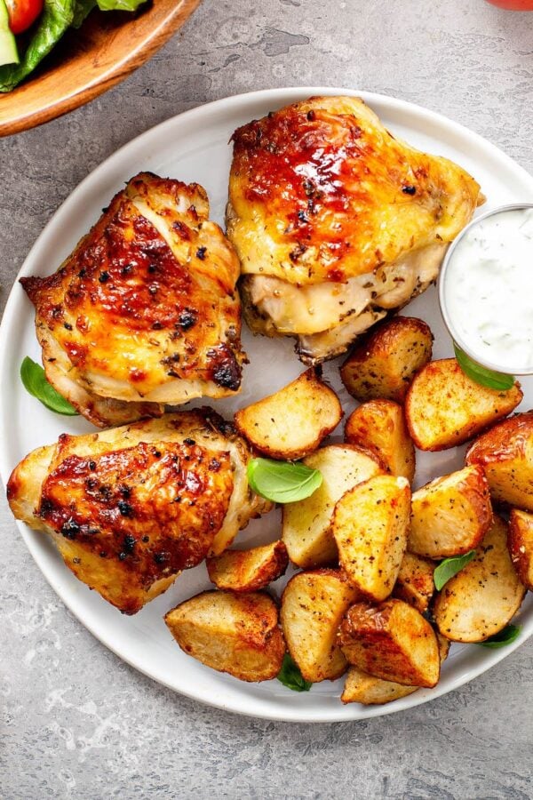 Baked chicken thighs on a white plate with roasted potatoes.