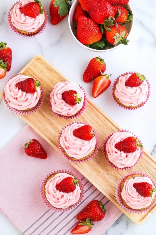 Strawberry cupcakes photographed from above with strawberries scattered about. 
