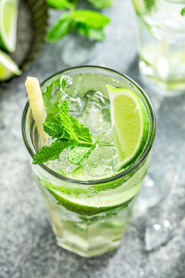 Up close image of the top of a mojito with lime and mint on top with a sugar cane stick.