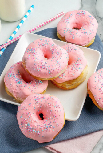 A plate of strawberry glazed donuts served with glasses of milk.