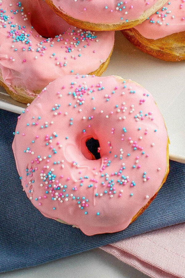 Close up image of a strawberry glazed donut topped with sprinkles. 