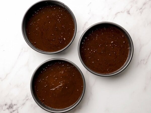 Three cake pans are filled with chocolate cake batter. 