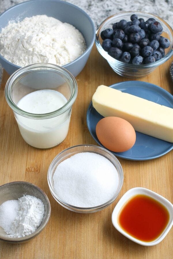 A wooden board with butter, sugar, cream, flour and blueberries.