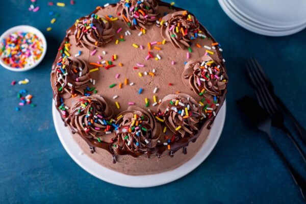 Up close image of the top of chocolate cake with sprinkles and chocolate sauce on top. 