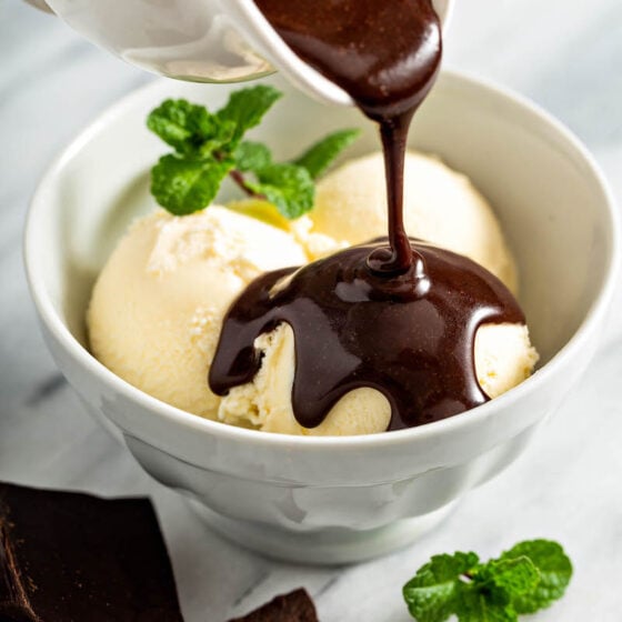 Chocolate sauce being drizzled on top of ice cream in a bowl.