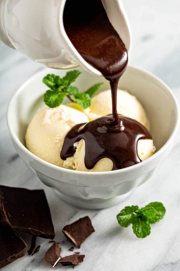 Chocolate sauce being drizzled on top of ice cream in a bowl. 