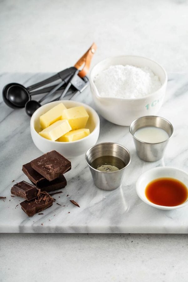 Ingredients in bowls for chocolate sauce on a marble countertop. 