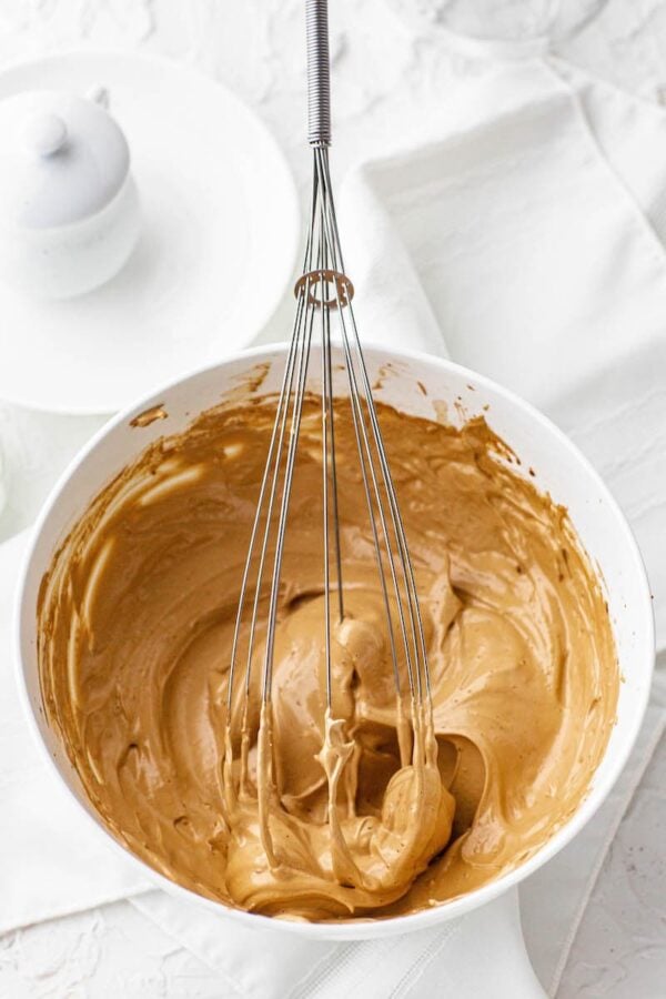 Whipped coffee topping for dalgona coffee in a white bowl with a large whisk.