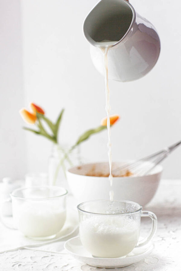 Milk being poured over ice in a glass mug.