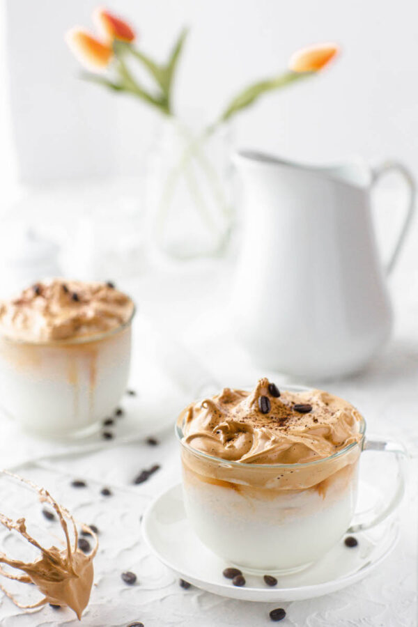 Two glass mugs filled with Dalgona coffee with saucers and espresso beans.