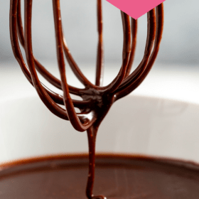 A whisk covered in chocolate sauce dripping over a bowl