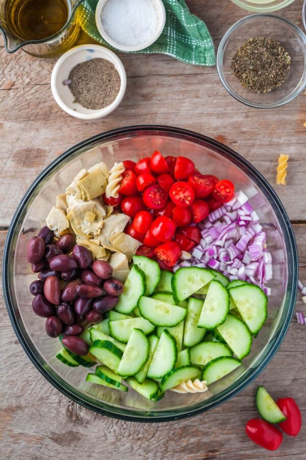 The ingredients for Greek pasta salad in a clear bowl.