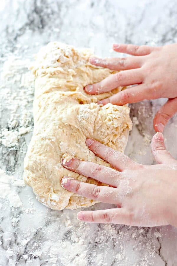 Hands kneading bread dough on a marble counter.