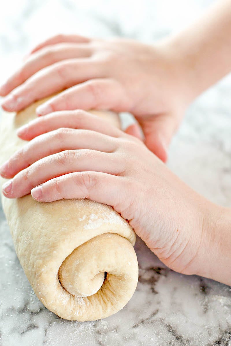 Rolled bread dough on a counter top with two hands rolling it 