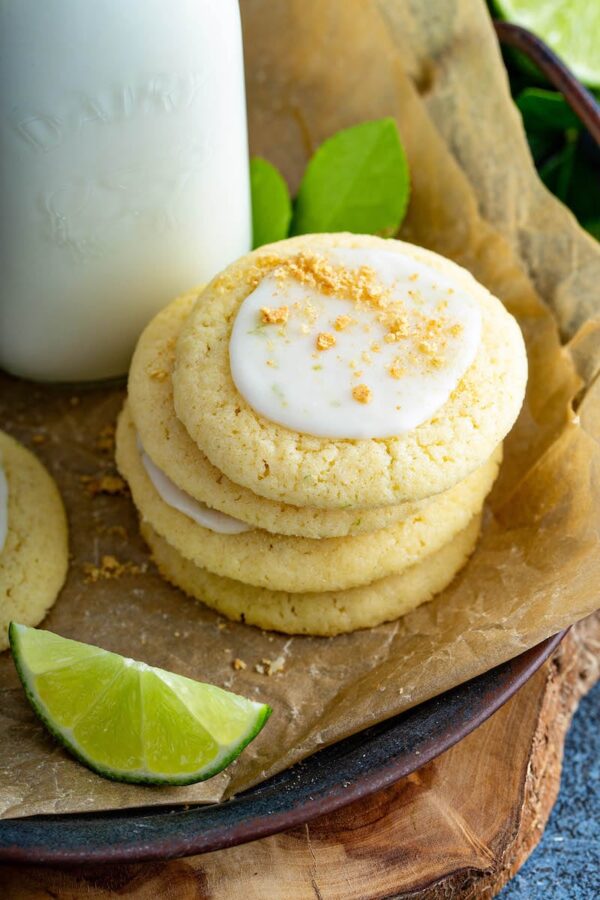 Stack of key lime cookies on parchment paper with milk and slices of limes.