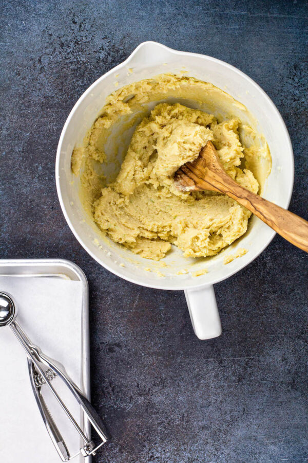 A bowl of cookie dough with a spoon in int and a cookie dough scooper to the side.