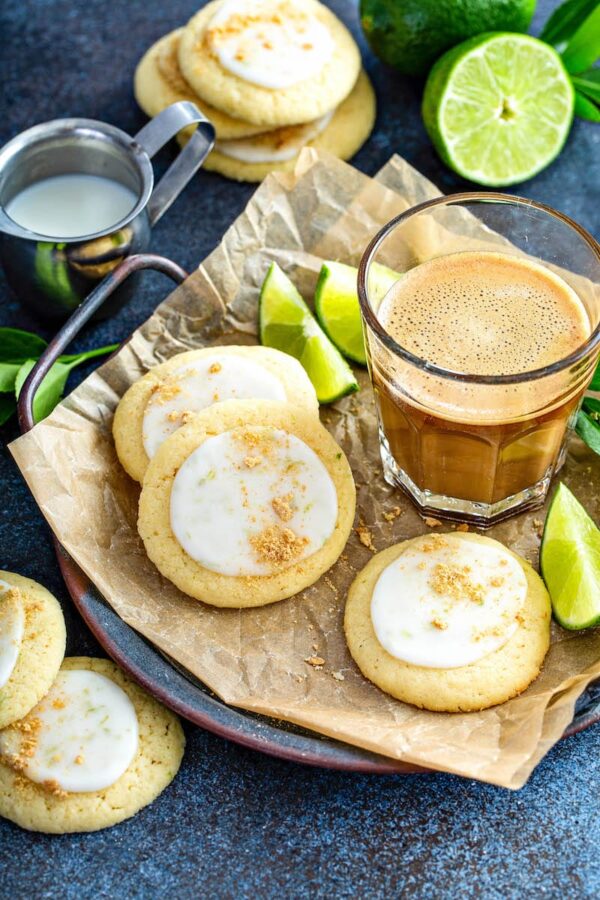 Key lime cookies on a plate with fresh limes and a cup of coffee.