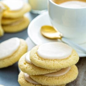 Vanilla meltaway cookies stacked on a plate with a cup of coffee and a gold spoon.
