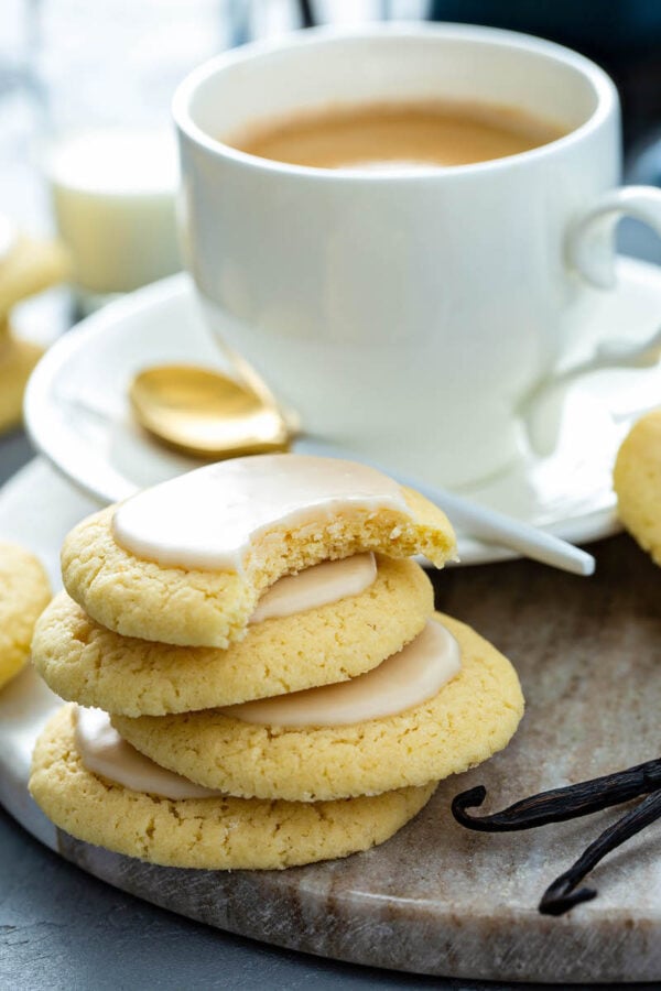 Vanilla meltaway cookies stacked on top of each other with a bite taken out of the top one and a cup of coffee in the background.