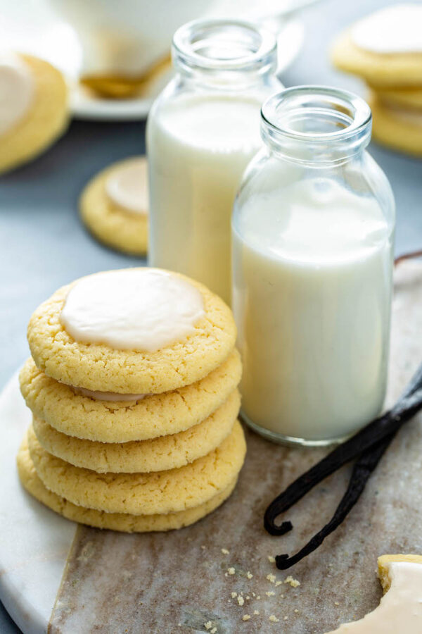 A stack of vanilla meltaway cookies on a stand with vanilla beans and two glasses of milk. 