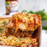 Ravioli Lasagna in a casserole dish sliced and being pulled out with a spatula.