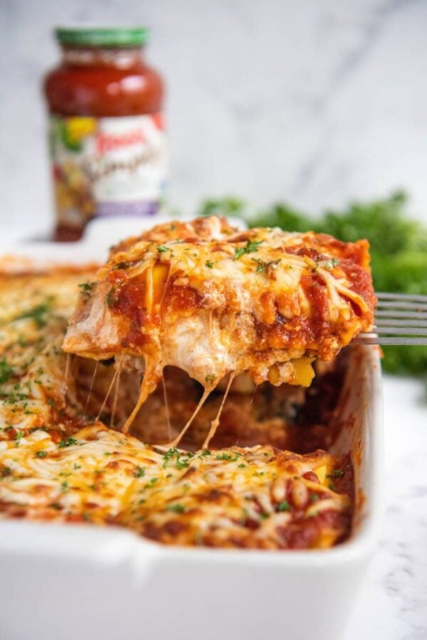 Ravioli Lasagna in a casserole dish sliced and being pulled out with a spatula.