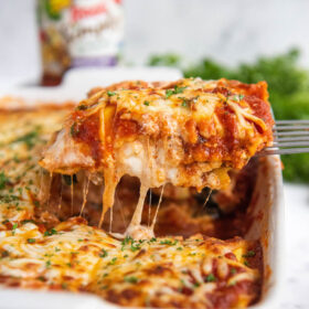 Ravioli Lasagna in a casserole dish sliced and being pulled out with a metal spatula.