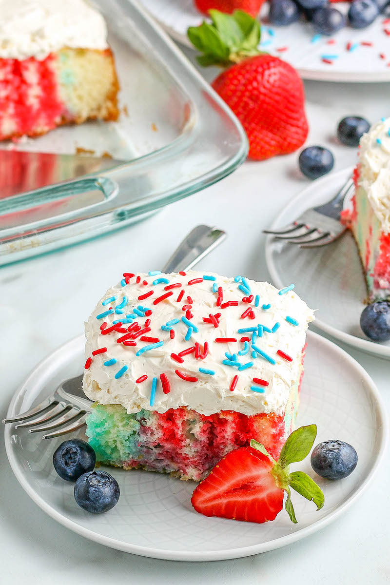 4th of July Cake on a white plate with fresh fruit and a fork.