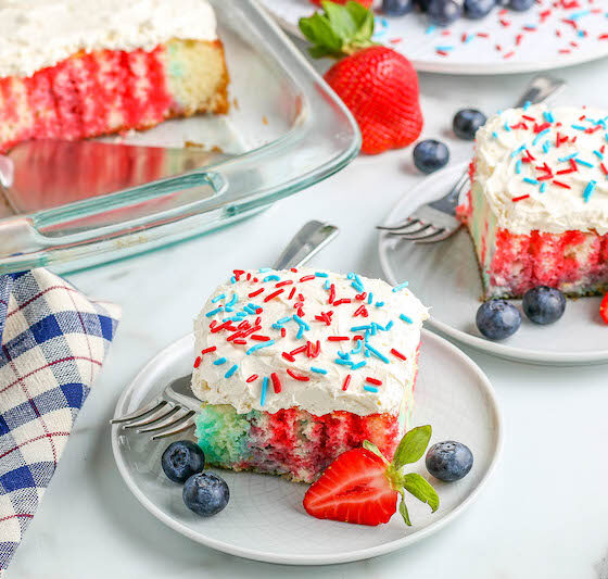 Two patriotic cake slices on plates with fresh fruit.