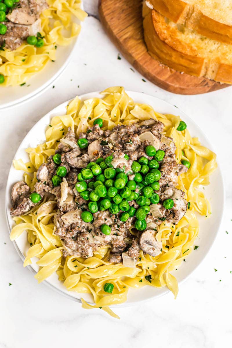 Beef Stroganoff on a plate topped with green peas. 