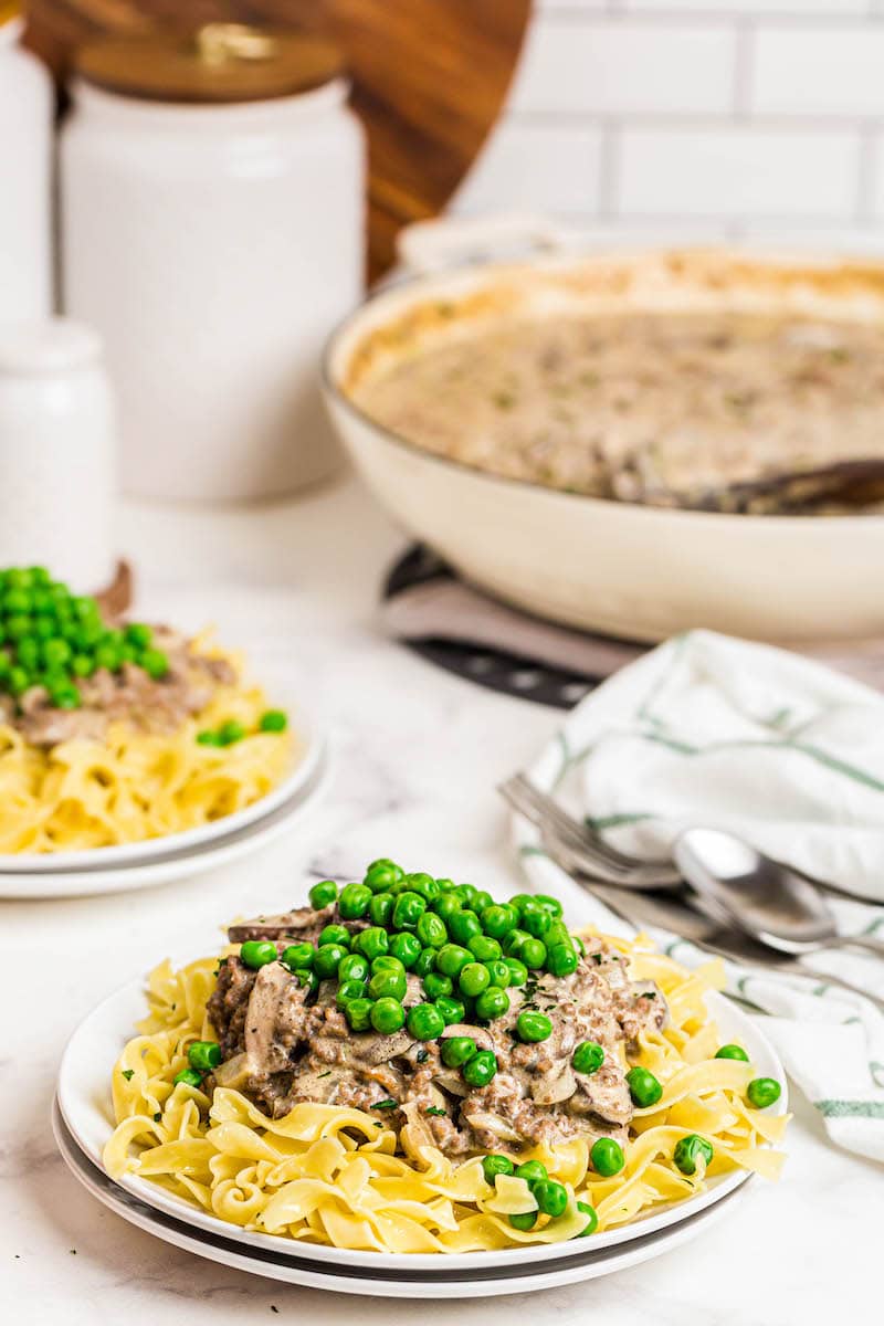 Two plates with egg noodles, creamy beef and mushrooms and peas.