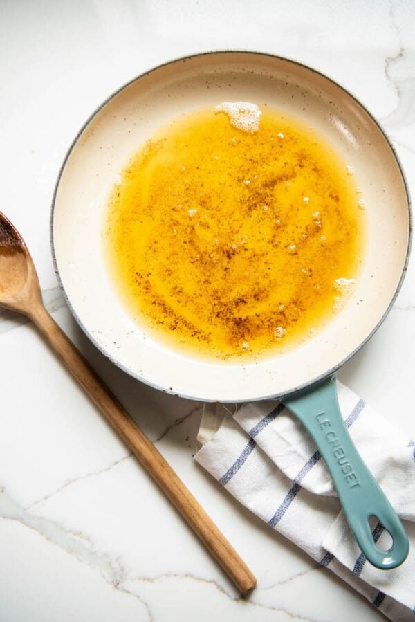 Brown butter in a skillet with a wooden spoon and towel.