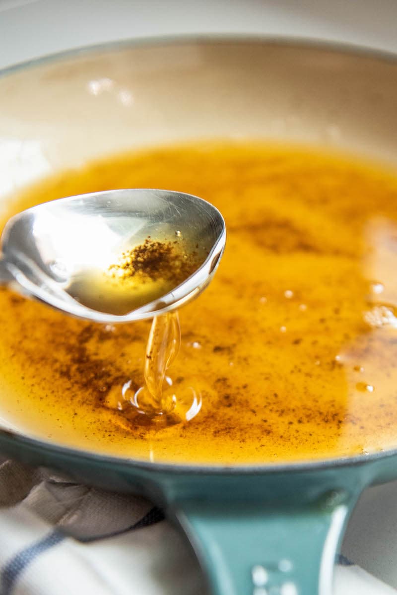 Butter in a skillet with spoon pouring some in.