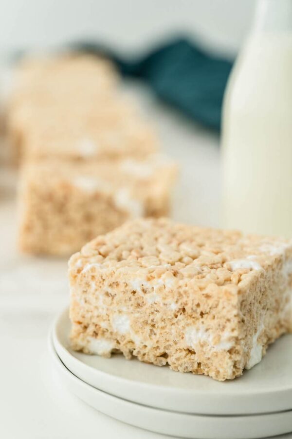 Rice krispie bar on a white plate with a cup of milk behind it.